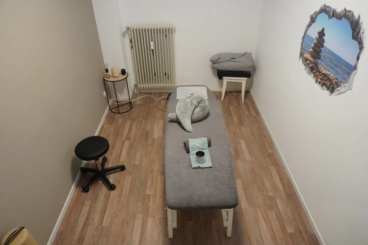 Behandlungsraum mit Therapieliege, Rollhocker und Wandbild mit Steinen